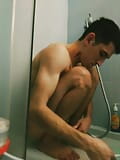 Sputare un giovane ragazzo etero snello e atletico con un tatuaggio si fa una doccia, si lava la testa e le gambe del pene nella toilette de snapshot 3