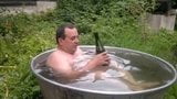 Naked old man rolls around in outside bath tub. snapshot 2