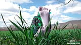 Des pieds de déesse dans de jolies chaussettes blanches avec un jean sur le champ d’herbe de printemps snapshot 9